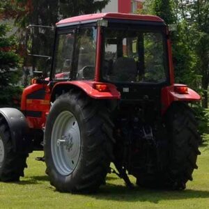 Tractor agricol rosu pe gazon, cu copaci in fundal